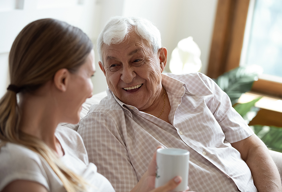 Smiling older man and caregiver talking at home, reflecting shared-home care for the Medicaid waiver payment tax exclusion.