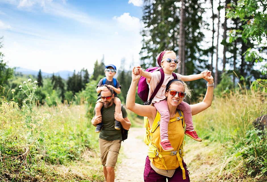 Parents carrying their children on a summer hike, representing families navigating kiddie tax rules for a child’s unearned income.