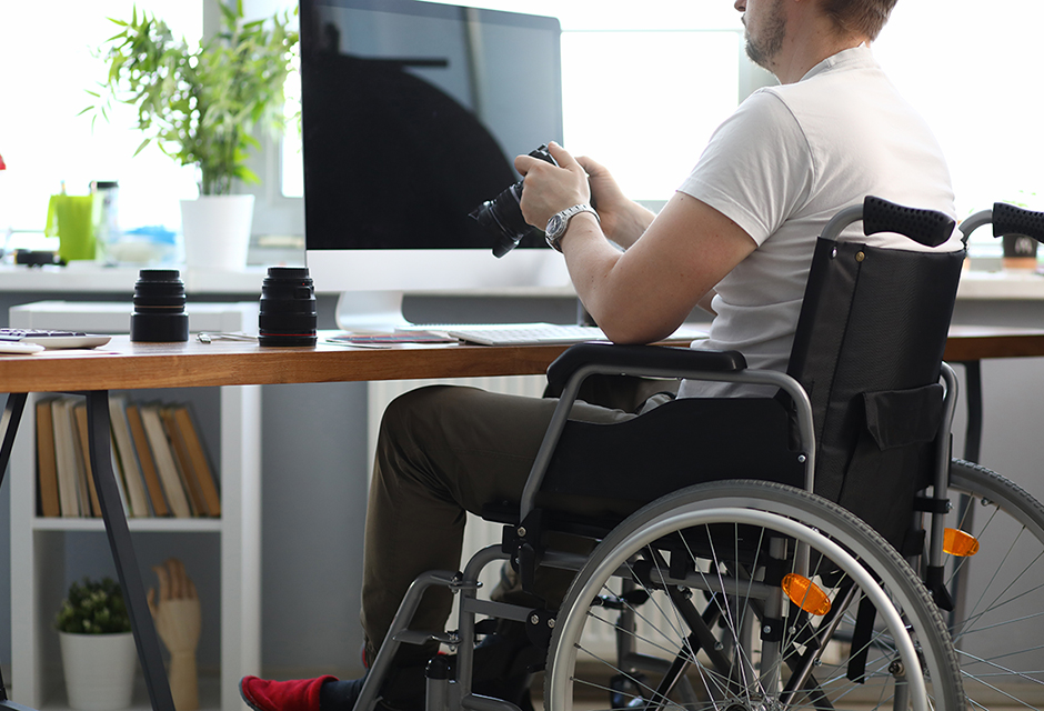 Content creator in a wheelchair holding a camera at a computer, illustrating tax reporting for influencer income and brand partnerships.