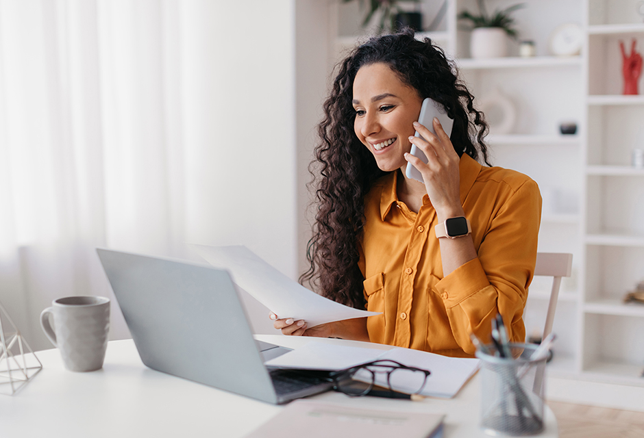 Woman reviewing paperwork beside a laptop during a phone call, illustrating a year-end tax planning conversation.