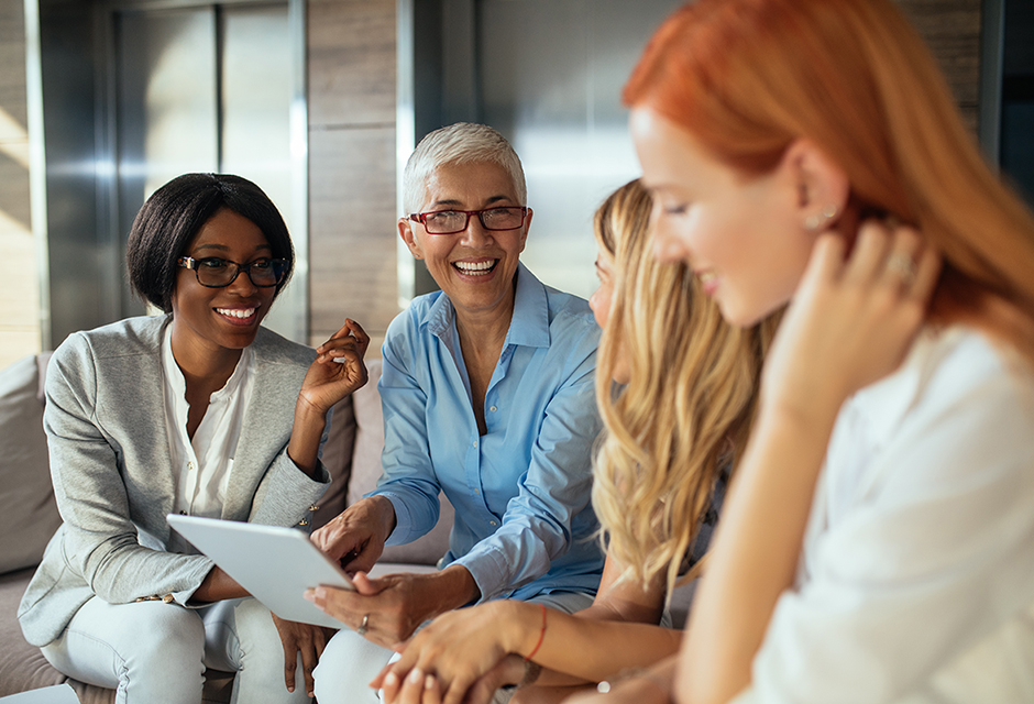 Four women collaborate around a tablet, celebrating women-owned tax and accounting businesses during National Women's Small Business Month.