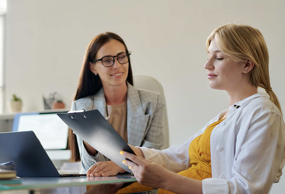 Two women review benefit documents during a discussion of the expanded paid family and medical leave tax credit for insured leave.
