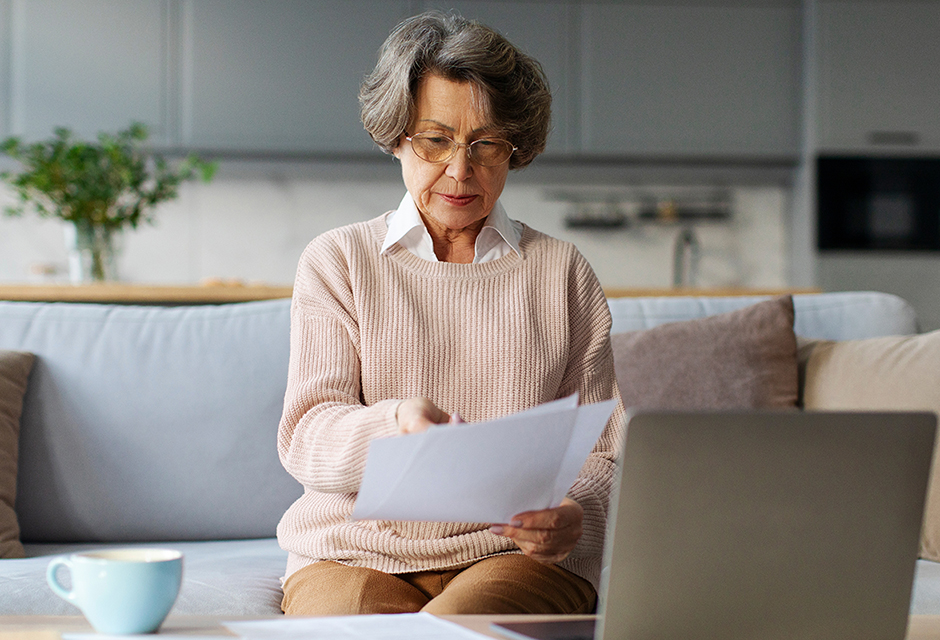 Older woman reviewing paperwork beside a laptop, illustrating the careful review needed for final-year beneficiary Schedule K-1 reporting.