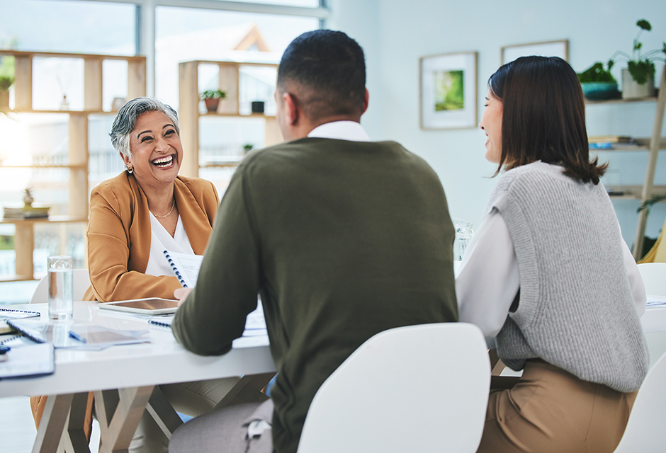 Smiling tax professional discusses retirement plan options with two small business clients during an office meeting.