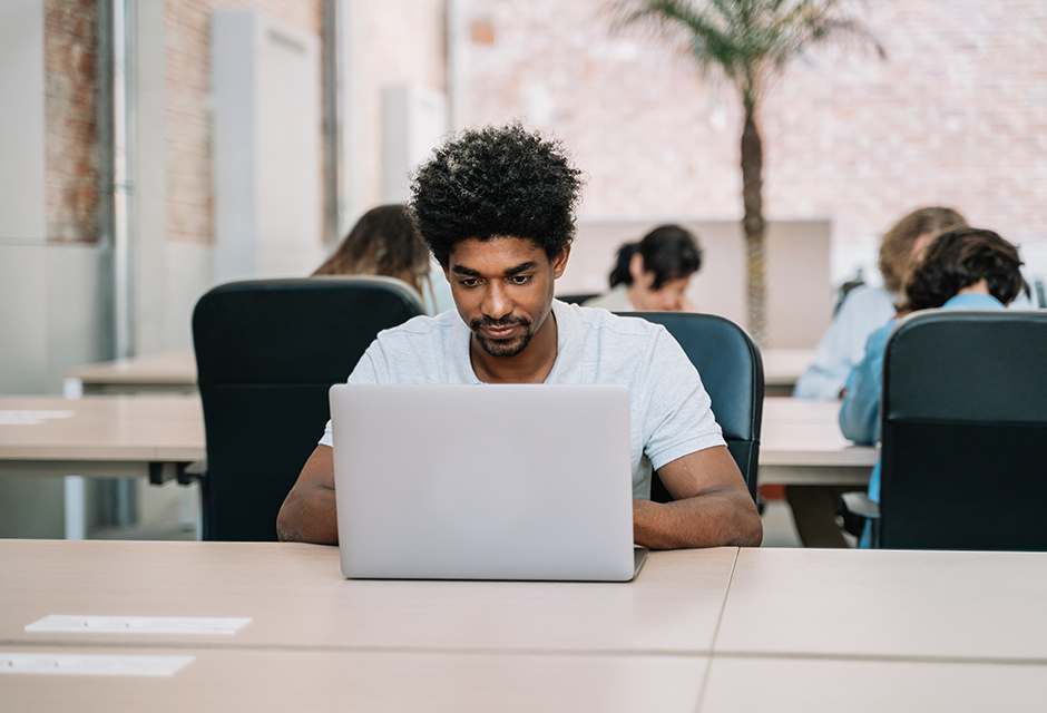 Man working on a laptop in a shared workspace, representing gig economy income and tax reporting.