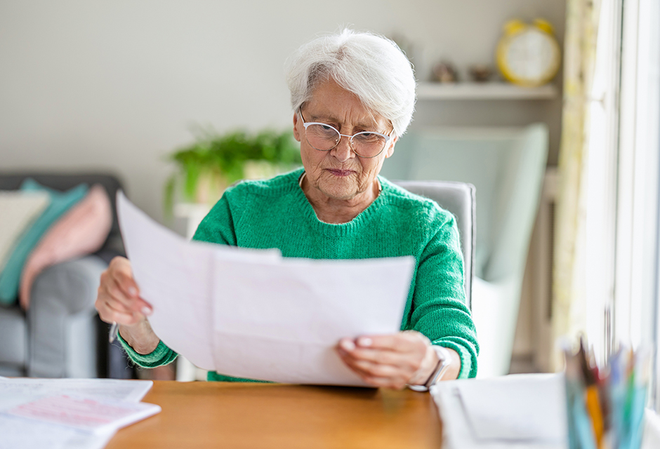 Older woman in a green sweater reviewing paperwork at home, illustrating the importance of accurate estate and trust beneficiary K-1 tax reporting.