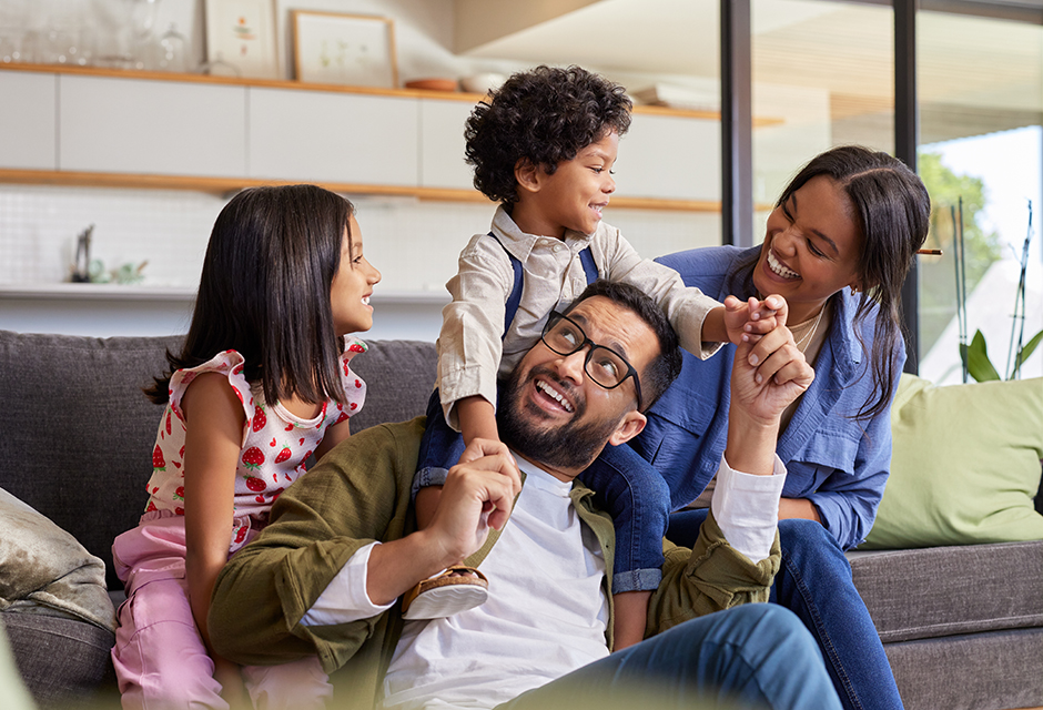 Two adults and two children laughing together at home, illustrating how gifts of stock to children can carry future tax consequences.