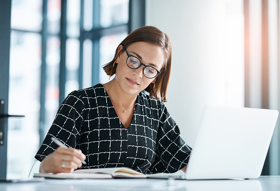 Tax professional reviewing qualified opportunity zone investment details in notes beside her laptop.