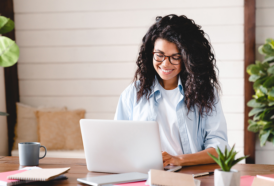 Smiling tax professional reviewing notes at her laptop while preparing for EA and PTIN renewal deadlines.