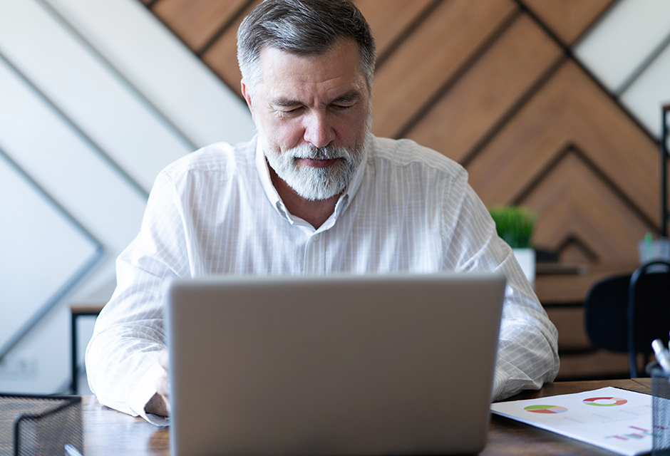 Tax professional reviews client books and financial reports on a laptop to prepare an accurate tax return.