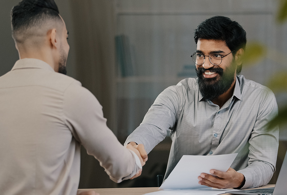 Tax professional greets a client while holding documents for a discussion about a projected midyear tax shortfall.