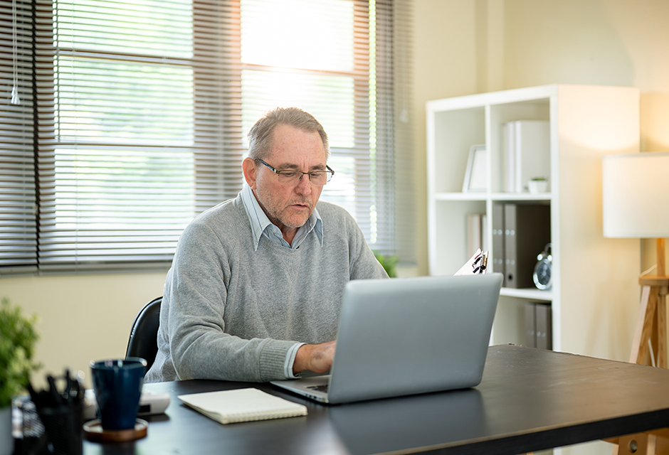 Man in a gray sweater reviewing tax information on a laptop, illustrating missed October tax filing deadlines and penalties.