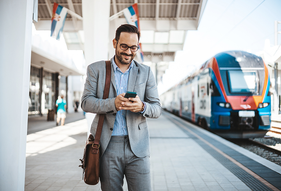 A business professional checks his phone at an international train station, illustrating U.S. tax reporting considerations for individuals working abroad.