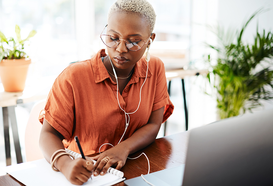 Adult tax professional takes notes beside a laptop during online AFSP continuing education.
