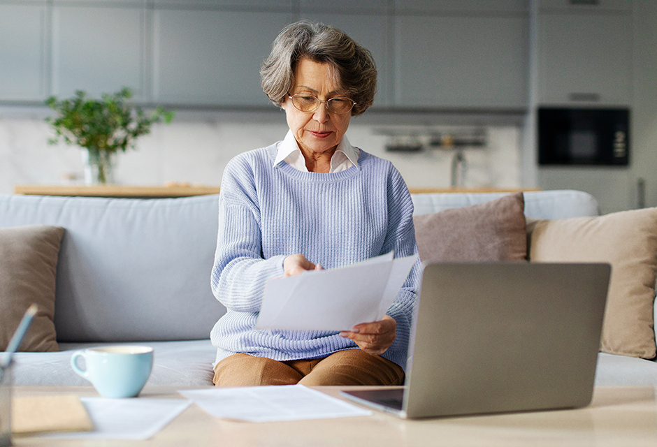 Older woman reviews tax documents beside a laptop while preparing to report beneficiary Schedule K-1 items on Form 1040.