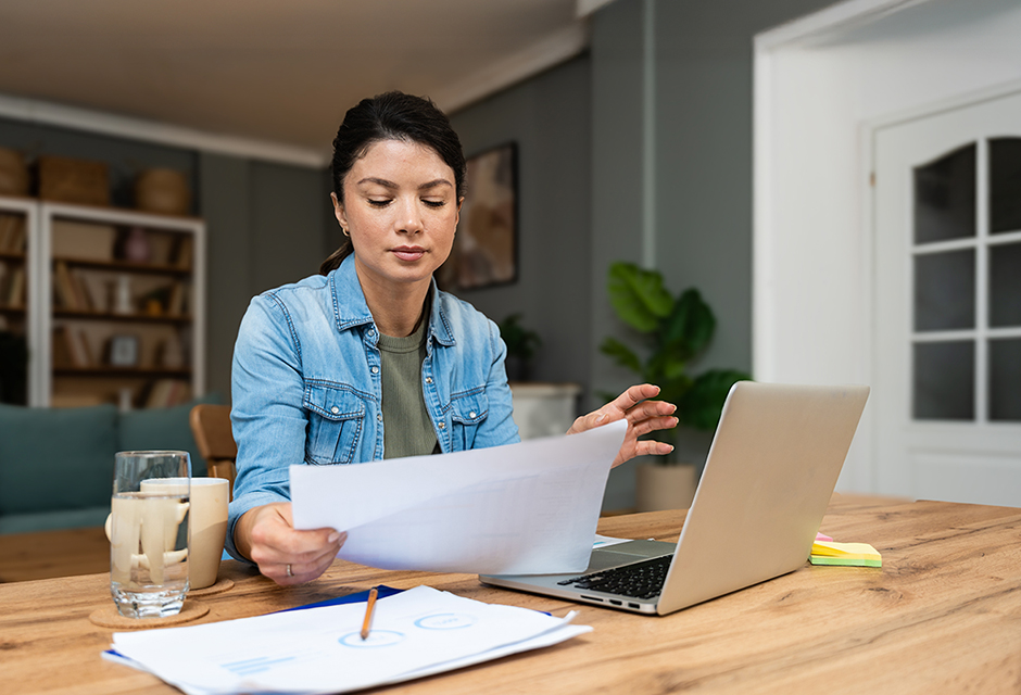 Woman reviewing paperwork beside a laptop, illustrating the reconciliation of online gambling records for accurate tax reporting.
