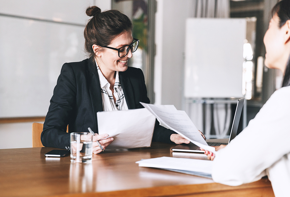 Woman reviewing financial documents with a colleague at an office desk, illustrating year-end business tax planning discussions.