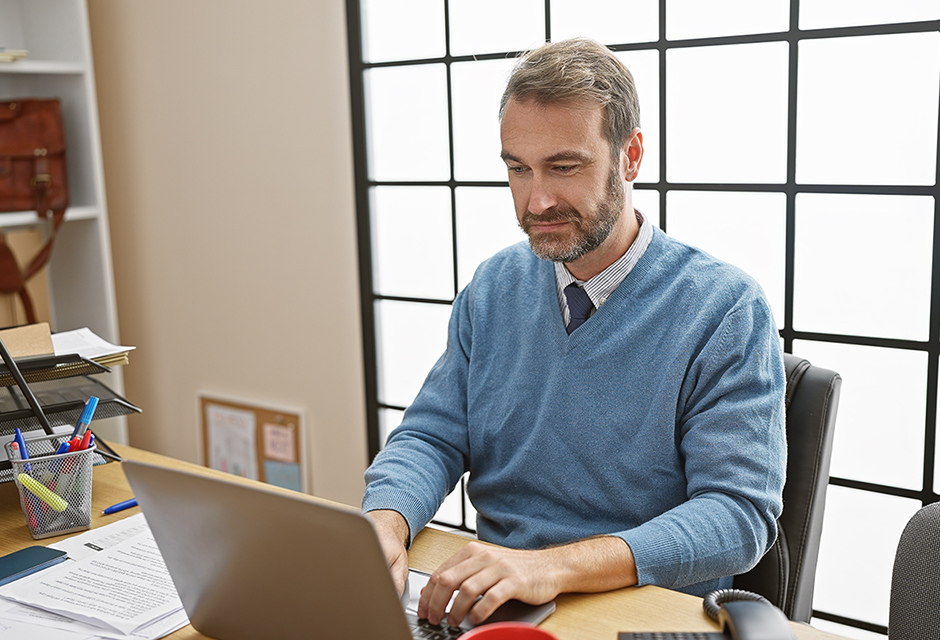 Tax professional working at a desk reviewing client information on a laptop as part of maintaining a written information security plan for data protection