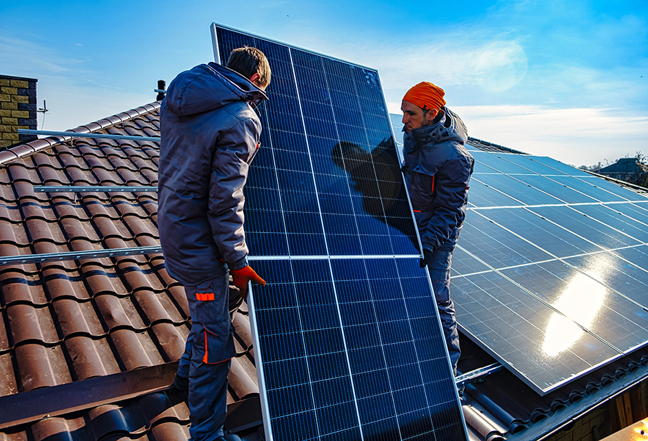 Two workers on a residential rooftop installing large solar panels, preparing the system for placement in service under updated energy credit rules.