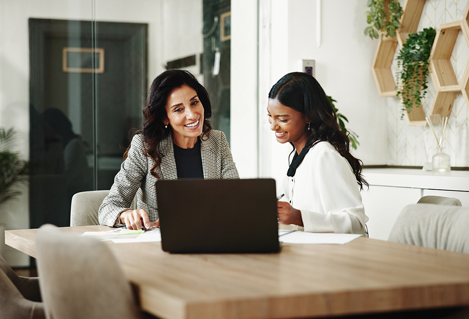 Two professionals reviewing business sale documents together at a laptop, discussing tax implications and structuring considerations for a client transaction.