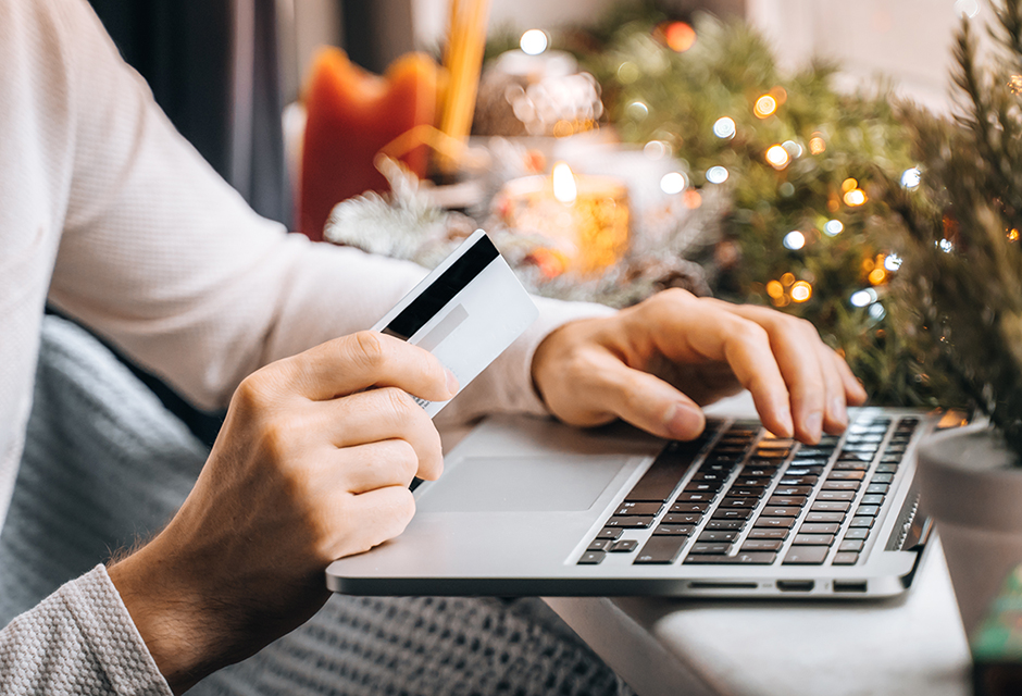 Person holding a credit card while shopping online on a laptop during the holidays, illustrating increased risk of gift card and IRS impersonation scams.